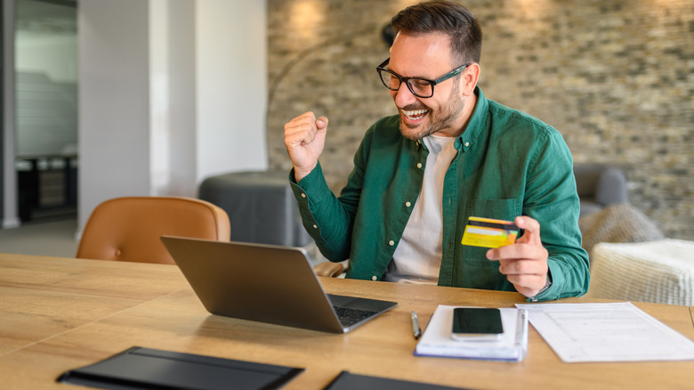 man holding credit card and looking at laptop