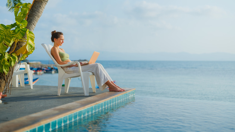 woman using a laptop while sitting by a pool