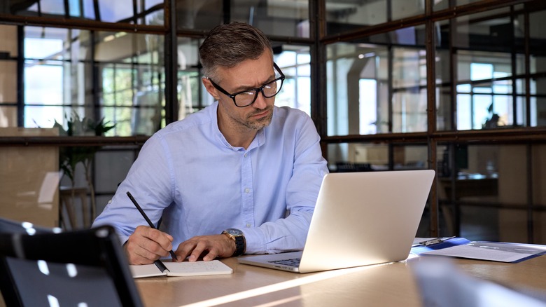 man taking notes next to laptop