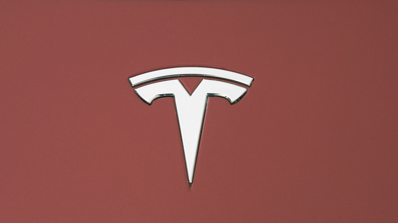 A closeup of the Tesla logo on a red Roadster.
