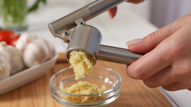 A metal press being used to crush garlic into small clear bowl