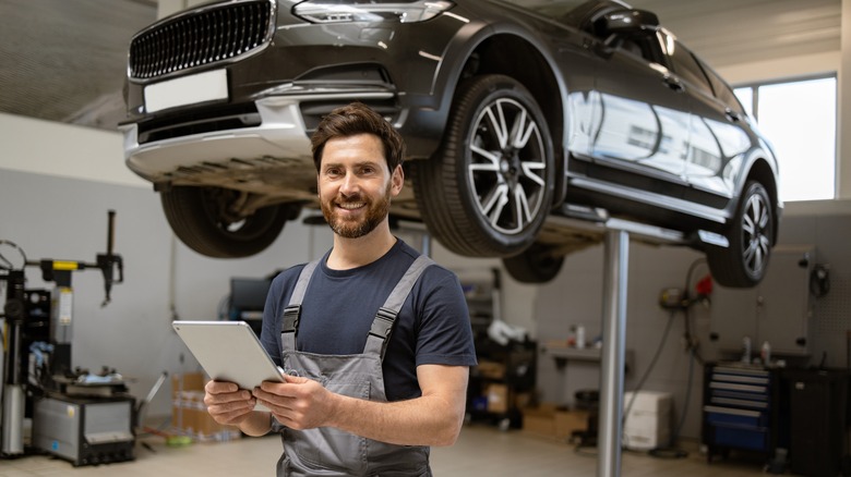 Friendly mechanic using tablet in modern car repair shop with car on lift.