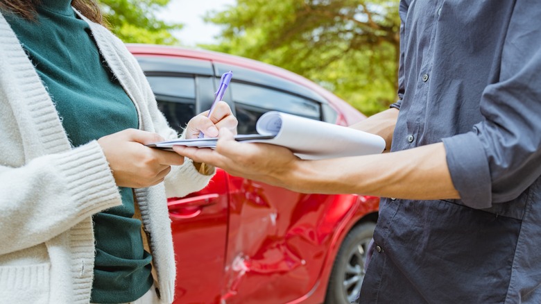 A woman signing a contract in front of a vehicle.