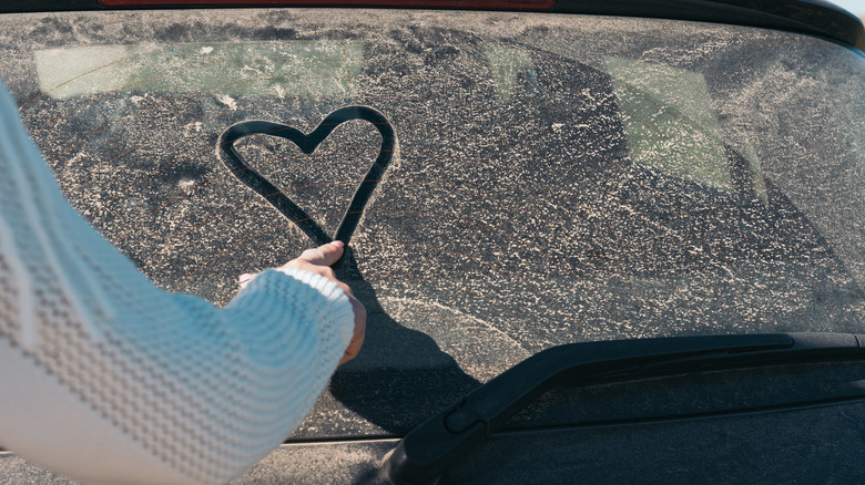 Young woman drawing a heart on a dusty car.