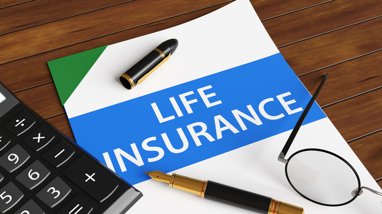 Bound life insurance service agreement, a golden fountain pen, a black calculator and spectacles on a wooden table.