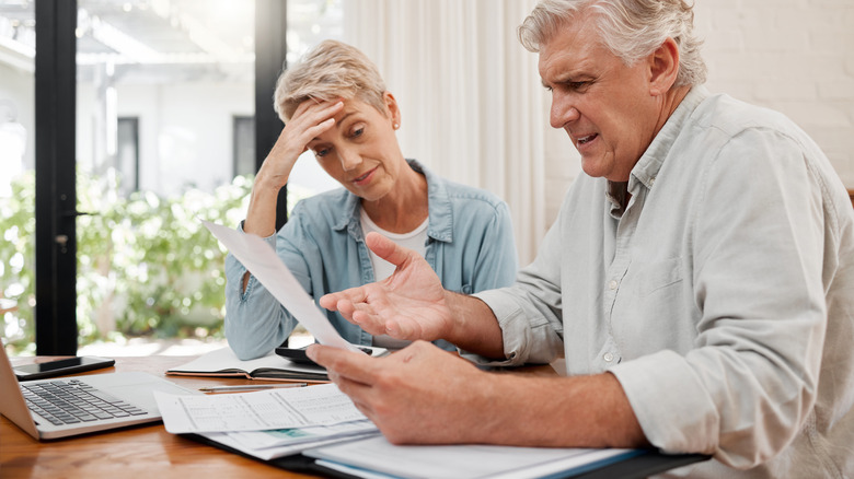 Upset mature couple sitting in front of laptop staring at paper