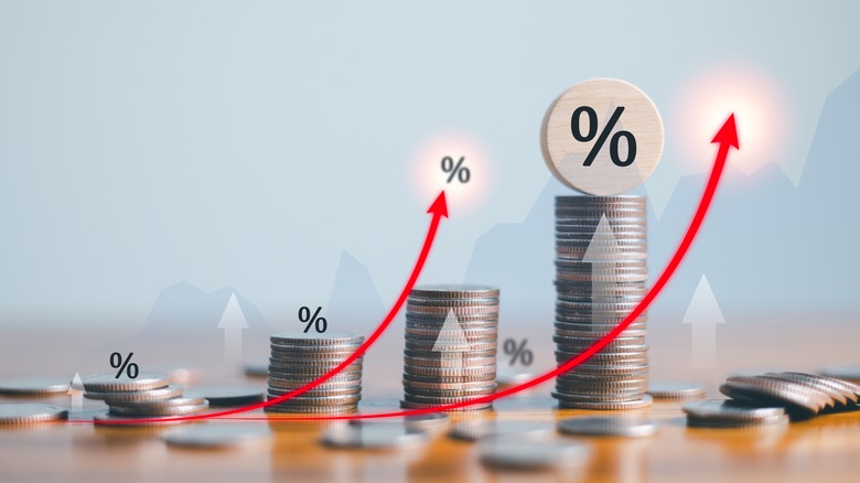 multiple stacks of coins behind white arrows with percentage icon on top and red arrows curving upward