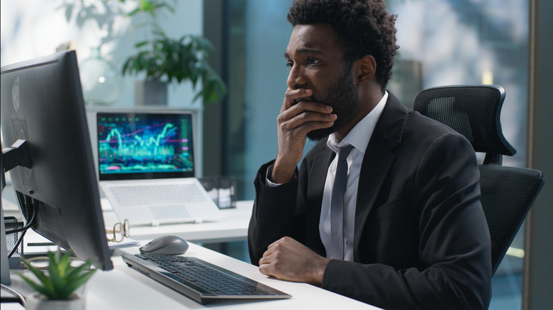bearded man wearing coat and tie with hand over mouth in shock as he stares at computer screen