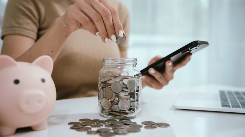 person putting coins in a jar with pink piggy bank