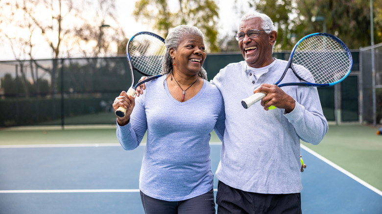 a senior couple playing tennis outside and smiling
