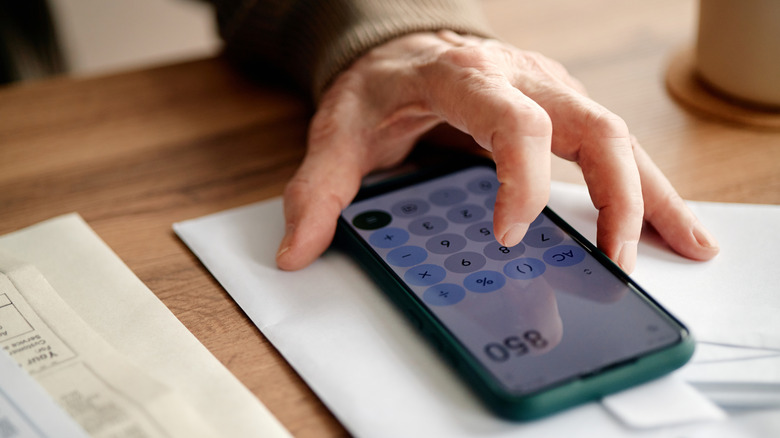 An older person's hand using a calculator on phone