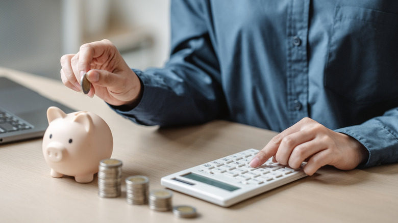 putting coins in piggy bank while using calculator