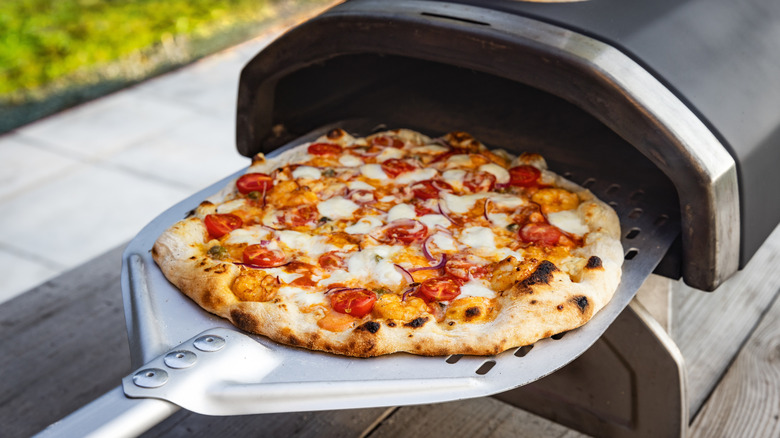 A pizza being carefully removed from an outdoor pizza oven