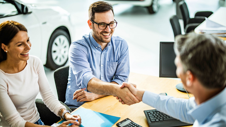 A smiling couple shaking hands with a salesperson
