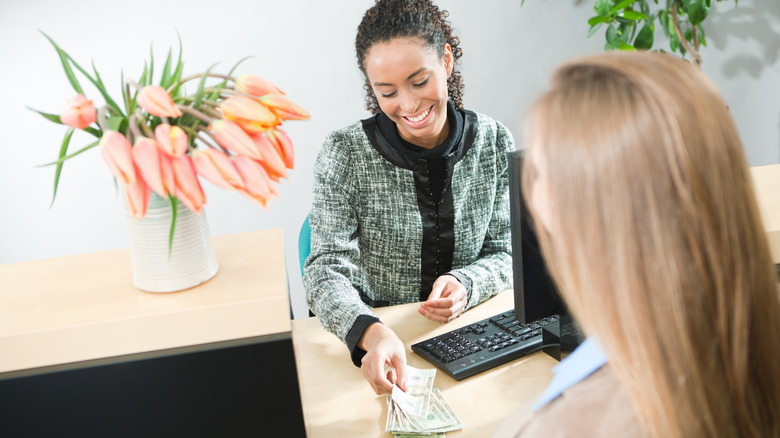 A smiling woman laying money on a desk