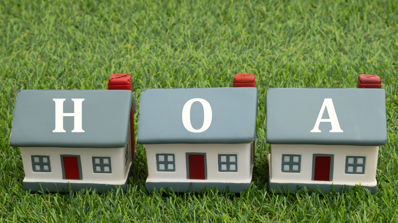 Three home figurines with the letters HOA, representing a homeowners association, on artificial grass.