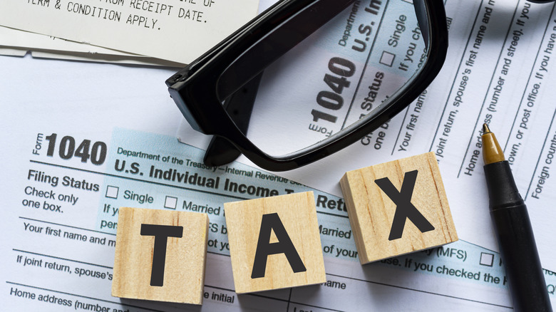 Wooden blocks with tax letters, reading glasses, pen, and 1040 tax forms