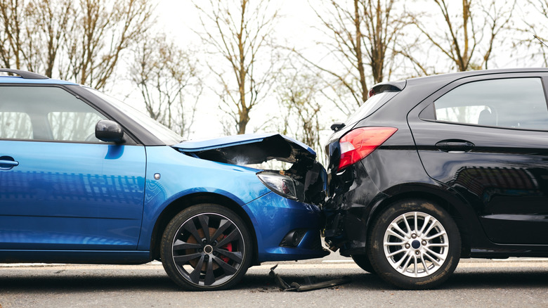Car accident scene with a blue vehicle crashing into a black car on the road.