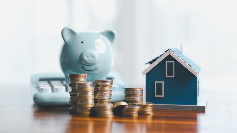 Stacks of coins placed in front of minature house and a piggy bank on a calculator