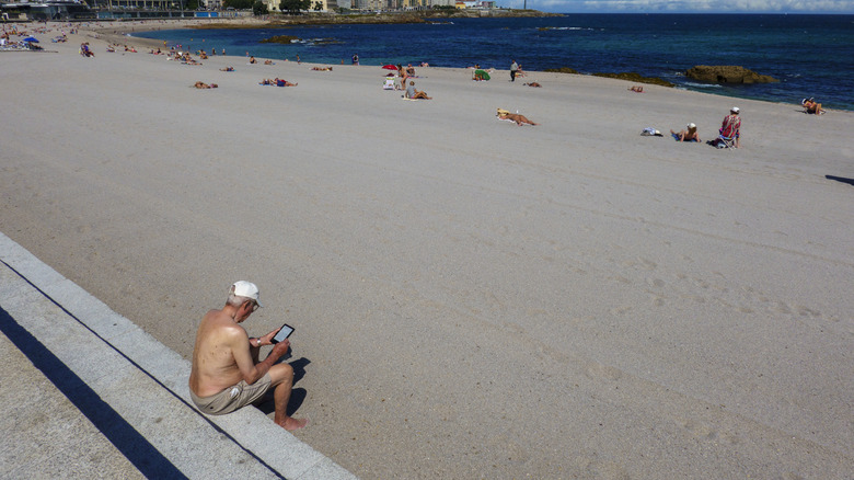 Older man sits using his tablet far away from others at the beach