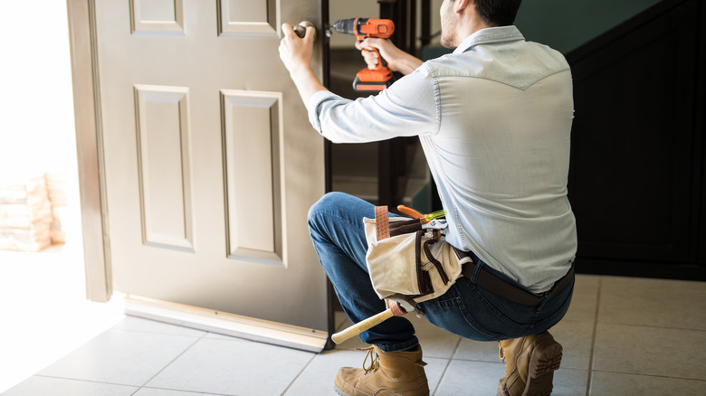 Repairman uses drill to repair the opened front door of a home
