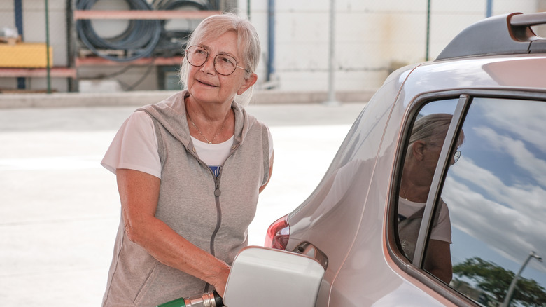 Elderly modern woman fills up her car at self-service fuel pump in European gas station.