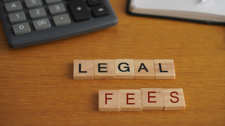 Wooden letters that spell out legal fees with calculator, notebook, and pen in the background.