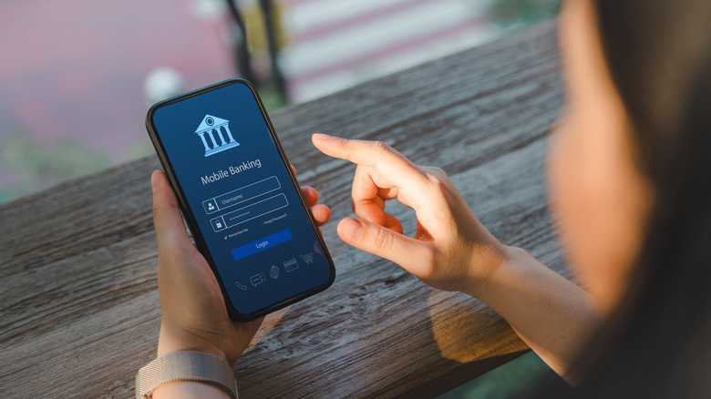 Over shoulder view of a woman accessing a mobile banking app on her smartphone.