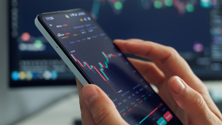 A person's hands hold a smartphone displaying a stock market chart with red and green candles.