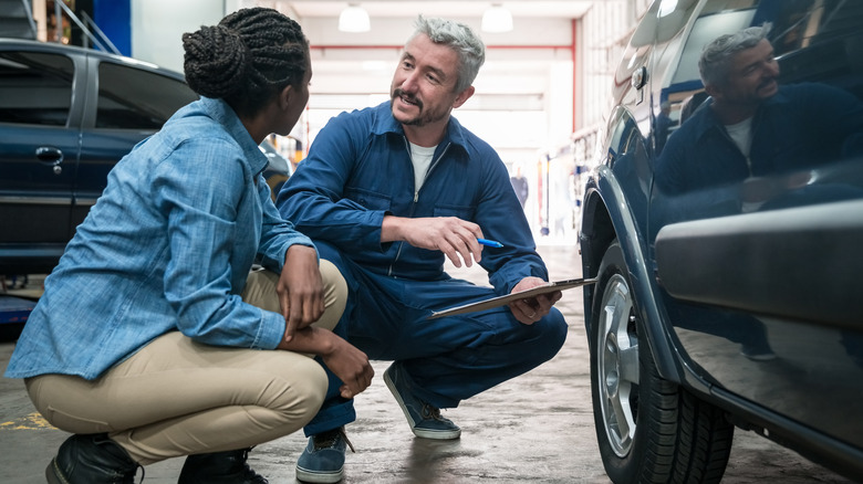 A man and woman crouching beside a vehicle