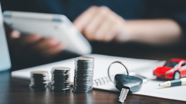 Stacked coins, car keys, and a model car on a table