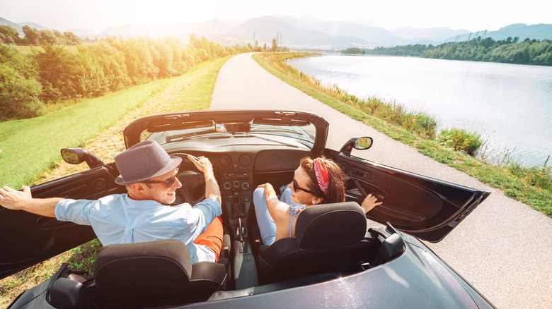 A couple in a convertible parked beside a lake