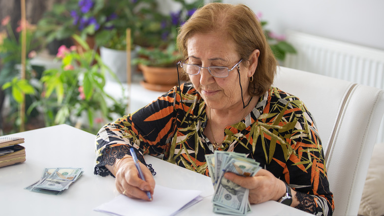 An elderly woman seated at a table counting money.