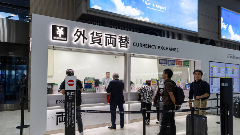 customers stand in line at an airport currency exchange booth