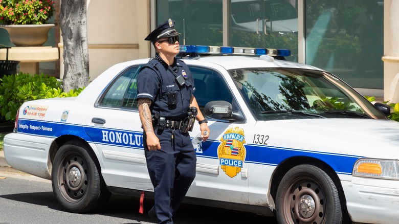 Honolulu police officer on duty by his patrol car.
