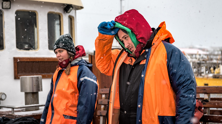 Tired man and woman fisherman stand on boat amid light snow