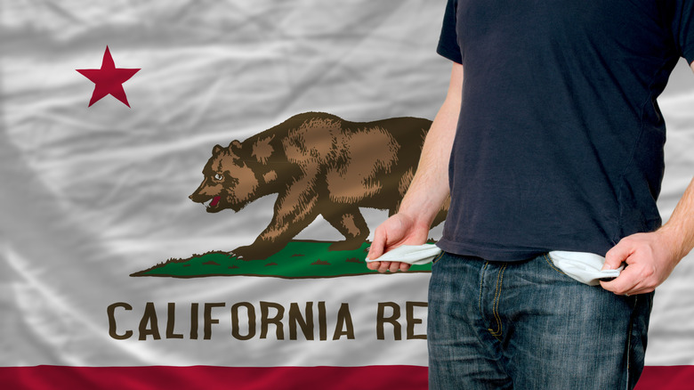 Man in T-shirt and jeans holds out empty pockets in front of California state flag