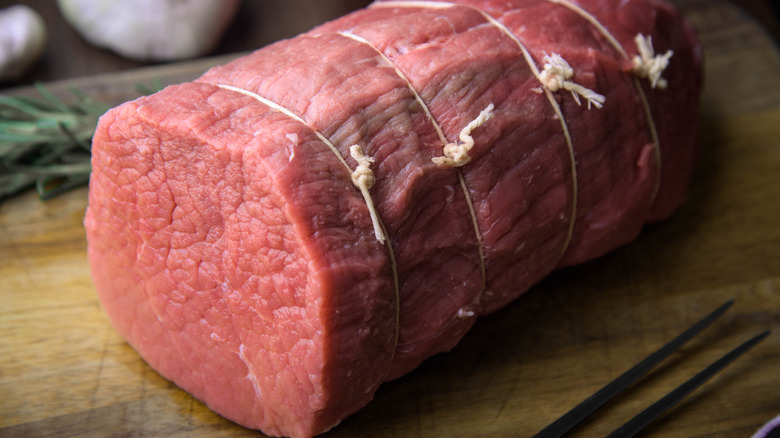 Angus beef eye round roast raw with butcher's twine and rosemary.