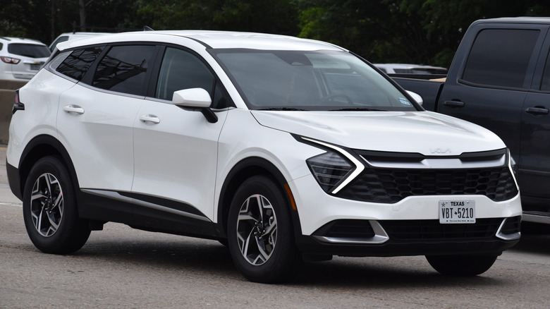 A white Kia Sportage traveling down a highway in moderate traffic.