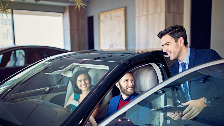 Car dealer is presenting a car to couple in the showroom