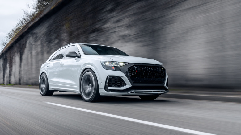 White Audi RS Q8 driving with a retaining wall in the background