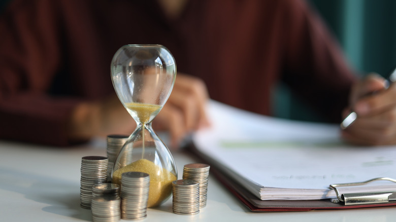 Person checking papers for income with piles of coins and hourglass.