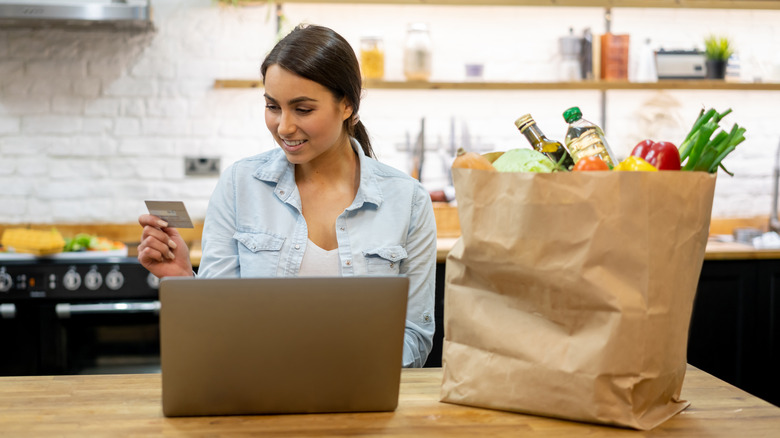 A woman smiling holding her credit card next to groceries