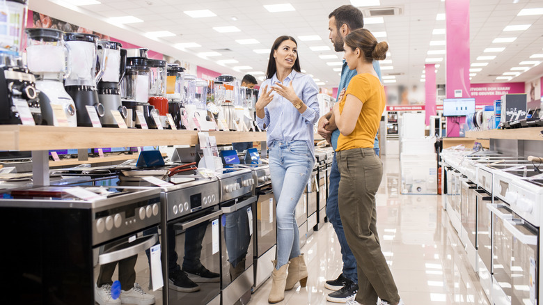 A salesperson shows ovens to an attentive couple