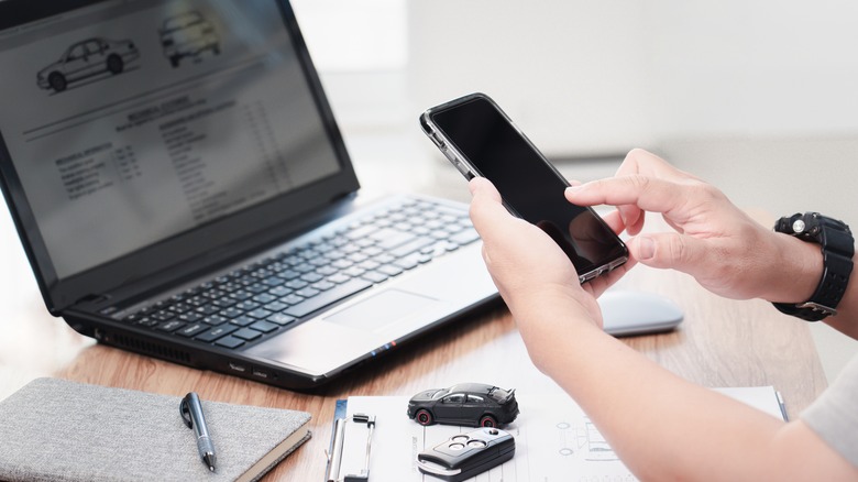 A man scrolling on his phone in front of his laptop