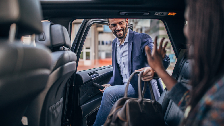 A smiling man holding a bag while entering a vehicle