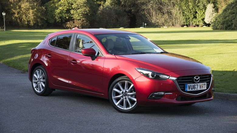 A red Mazda Mazda3 Hatchback driving down a road.