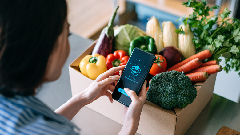 A woman holding a phone over groceries