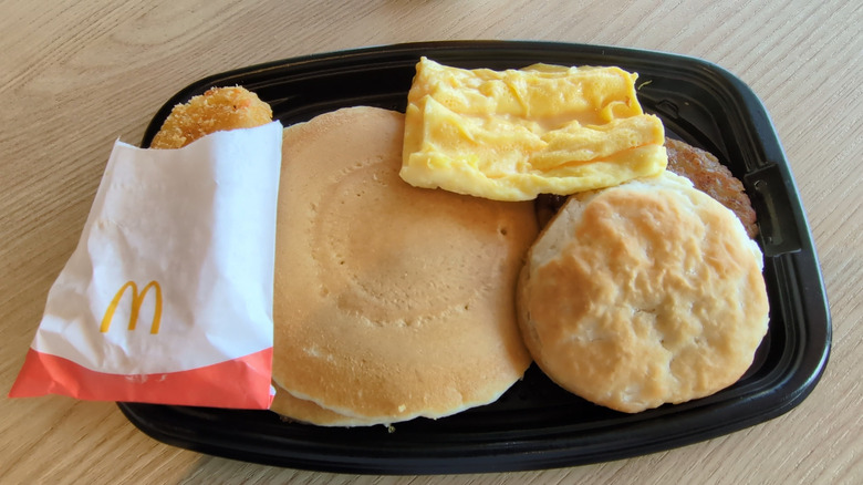 McDonald's Full Breakfast Meal with Hash Browns, Pancake, Scramble Egg, Biscuit, Sausage and a Coffee inside a McDonald's Restaurant