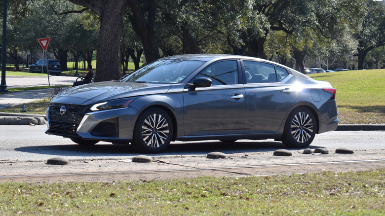 A Nissan Altima in metallic grey, traveling northbound between a Metro railway tracks and Hermann Park reserve.